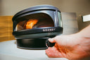 A hand adjusts the front control dial of an Off Black Gozney Arc Lite with a gas flame inside.
