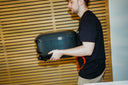 A man carries an Off Black Gozney Arc Lite beside a timber slat wall.
