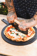 Gozney Pizza Rocker with a wooden handle cutting a margherita pizza