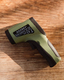 Green and black Gozney infrared thermometer resting on a sunlit wooden surface.