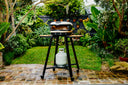 Bone Gozney Arc XL on a Gozney Arc Stand with wooden side shelves in a leafy garden