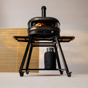 Off Black Gozney Dome Gen 2 burning on a wheeled stand with wooden side shelves and a covered gas bottle.