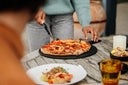 Gozney Pizza Cutter with a wooden handle being used to slice pizza on an outdoor table