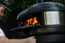 A person adjusts the front control of an Off Black Gozney Dome Gen 2 oven with flames inside.