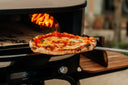 Margherita pizza on a peel in front of a Bone Gozney Dome Gen 2 oven with a wood fire burning inside.